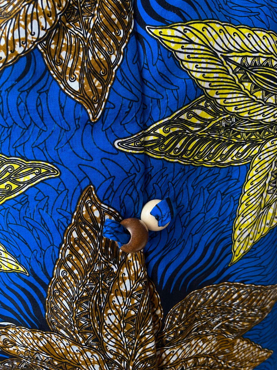 Close-up of a blue patterned fabric with large brown and yellow tropical leaf motifs and a small round wooden button.